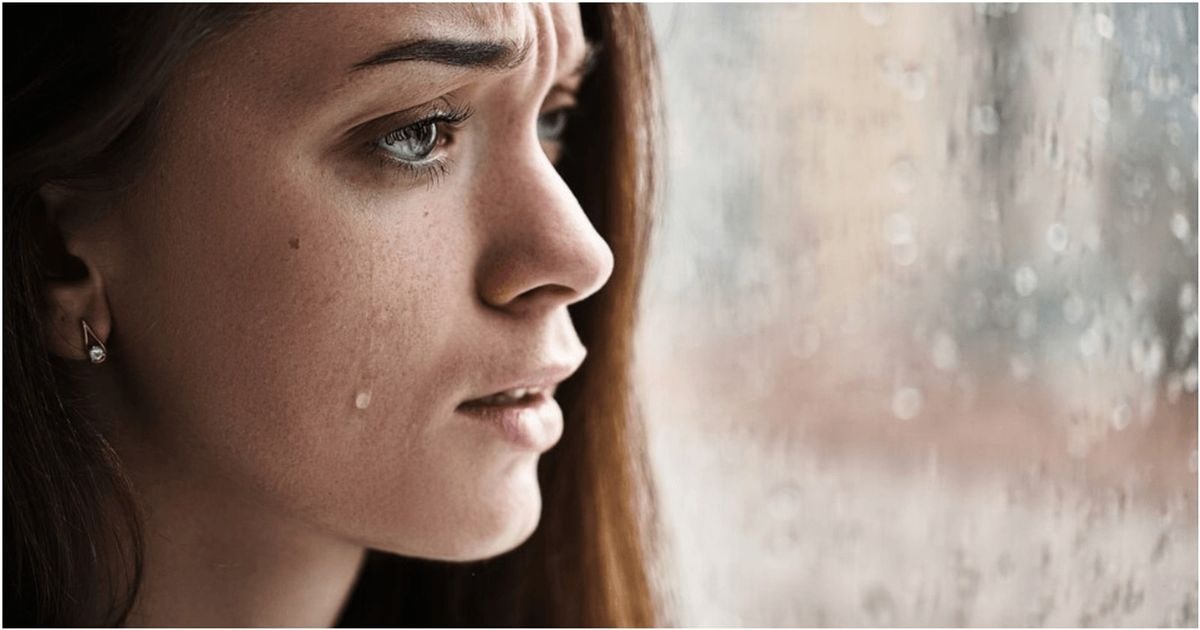 Vieniša mergina jaučiasi liūdna žiūrėdama pro langą, už kurio lyja lietus