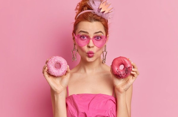 woman with pink outfit posing with two pink donuts