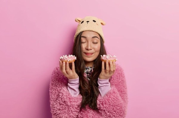woman with closed eyes holding two donuts