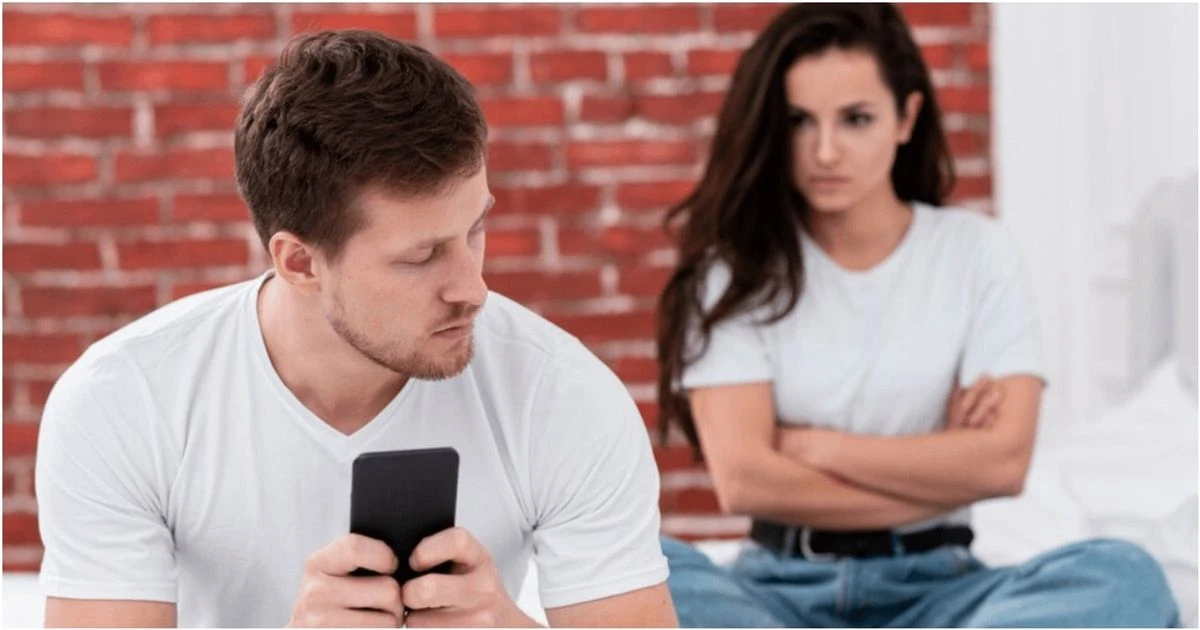 Pavydi moteris piktai žiūri į savo vaikiną, laikantį telefoną